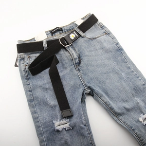 Détail d'une ceinture en toile noire avec double anneau en D argenté sur un jean bleu clair