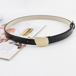 Close-up of slim black leather belt with a geometric gold buckle over a magazine background