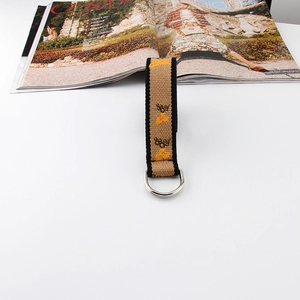 Detailed close-up of woven canvas belt featuring yellow bee embroidery and silver D-ring