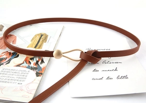 Détail d'une ceinture fine marron caramel avec boucle dorée et design de nœud élégant