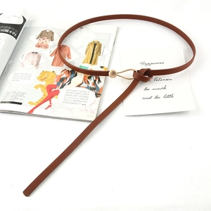 Détail d'une ceinture fine en cuir marron avec boucle crochet dorée et bouton décoratif