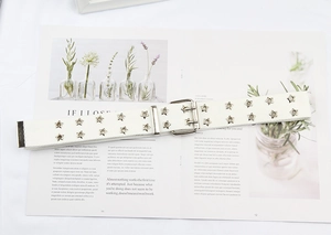 Detail view of white canvas belt with silver star eyelets and a double-prong buckle