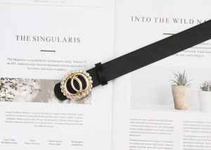 Détail d'une ceinture en cuir noir avec une boucle dorée à double anneau et strass