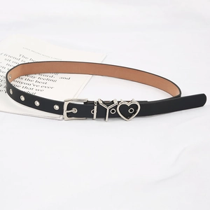 Détails d'une fine ceinture en cuir noir avec des breloques en cœur et des œillets
