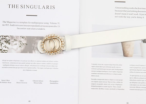 Détail d'une ceinture en cuir blanc avec boucle double anneau dorée ornée de strass brillants