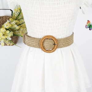 Close-up of bohemian woven straw belt with a large circular buckle on a white dress