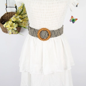 Detail of woven bohemian belt with round wooden buckle on white pleated dress