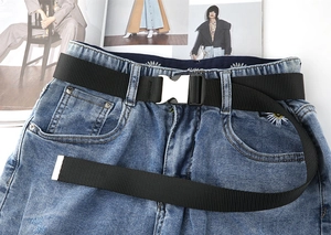 Nahaufnahme des schwarzen Nylon-Taktikgürtels mit Metallschnalle auf Jeans mit Gänseblümchen