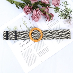 Detail view of woven herringbone belt featuring a bright orange circular wood-textured buckle