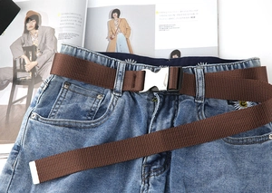 Detail eines kaffeebraunen gewebten Taktikgürtels mit Silberschnalle auf blauer Jeans