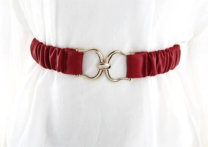Dettaglio di cintura elastica rossa con fibbia a morsetto dorata su un abito bianco