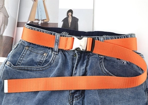 Detail eines leuchtend orangefarbenen Segeltuchgürtels mit Schnalle an blauer Jeans