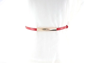 Détail d'une ceinture fine rouge avec boucle dorée rectangulaire sur vêtement blanc