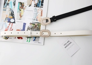 Détail de ceintures fines en cuir noir et blanc avec boucles ovales serties de perles