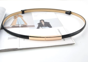Détail de la fine ceinture femme en cuir verni noir avec boucle rectangulaire dorée