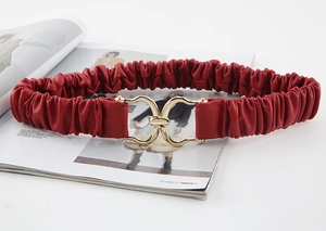 Dettaglio cintura elastica rossa con fibbia dorata a doppio anello su rivista di moda