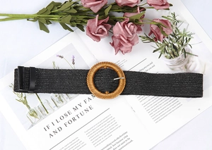 Detail of a black woven belt with a round straw buckle and leather loop over a magazine