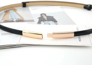 Détail d'une ceinture fine en cuir verni noir avec boucle métallique rectangulaire dorée