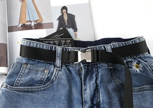 Detail einer blauen Jeans mit elastischem Bund, schwarzem Taktikgürtel und Gänseblümchen