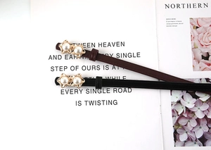 Detail of slim black and brown pearl belts with gold flower buckles on a magazine