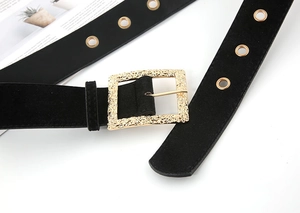 Close-up of black suede belt featuring a vintage gold textured square buckle and metal eyelets
