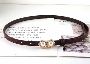 Detail of burgundy leather belt featuring gold abstract buckle with elegant pearl accents