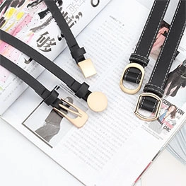 Detail of four thin black belts featuring various gold metal buckles on a fashion magazine
