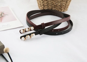 Detail of slim black and red waist belts with gold buckles featuring pearls and rhinestones