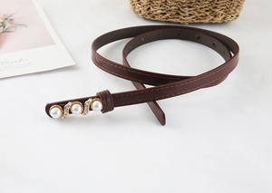 Macro detail of slim brown leather belt with gold buckle, pearls, and crystals