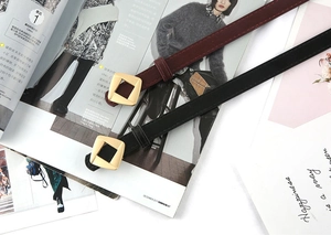 Detail of burgundy and black slim leather belts with gold square buckles on magazines