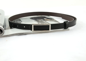 Close-up of minimalist black leather belt with rectangular silver buckle on fashion magazine