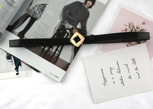 Close-up of slim black leather belt with a geometric gold buckle on a white cloth