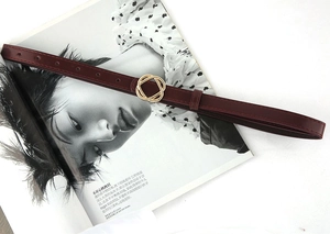 Detail of burgundy slim belt featuring a gold interlocking ring buckle on a fashion magazine