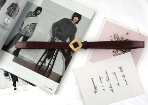 Close-up of a burgundy leather belt with a geometric gold metal buckle on a stylish desk