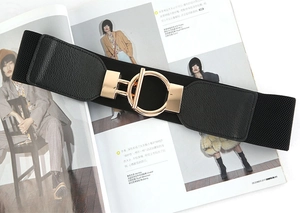 Detail of a wide elastic waist belt in black with a gold metal T-bar ring buckle closure