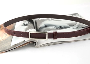 Close-up of minimalist burgundy leather thin belt with rectangular silver buckle on a magazine