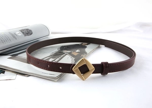 Detail of burgundy leather belt with a geometric gold rhombus buckle on white fabric