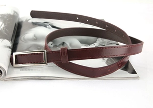 Detail view of burgundy slim leather belt with rectangular silver buckle on a magazine