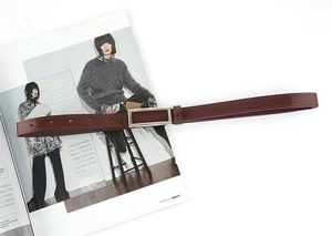 Detail of burgundy leather belt with silver rectangular buckle over a fashion magazine