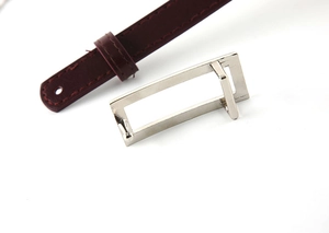 Close-up of polished rectangular metal buckle on slim burgundy leather belt