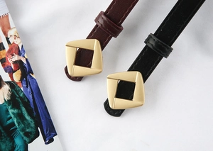 Close-up of golden geometric buckle on black and burgundy leather belts for women