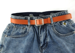 Detail van blauwe denim jeans met madeliefjes borduursel en een levendige oranje riem met gesp