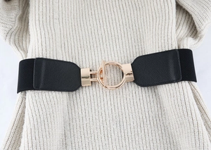 Detail of wide elastic black belt with gold circular metal buckle on beige dress