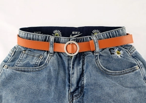 Detail van oranje slanke riem met zilveren gesp op blauwe jeans met madeliefjes borduursel