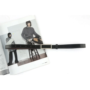 Elegant black slim leather belt with rectangular silver metal buckle on fashion magazine