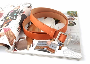 Detail van een smalle oranje leren riem met zilveren vierkante gesp op een tijdschriftachtergrond