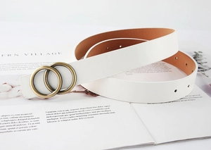 Détail d'une ceinture en cuir blanc avec doubles anneaux dorés sur un fond de magazine