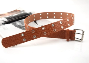 Detail of brown faux crocodile leather belt with double grommets and silver buckle