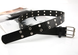 Detail of black crocodile texture belt with double row metal eyelets and silver buckle