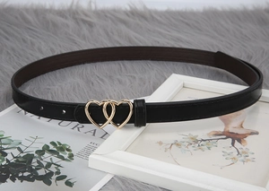 Close-up of elegant black slim belt with double heart golden buckle on soft grey background